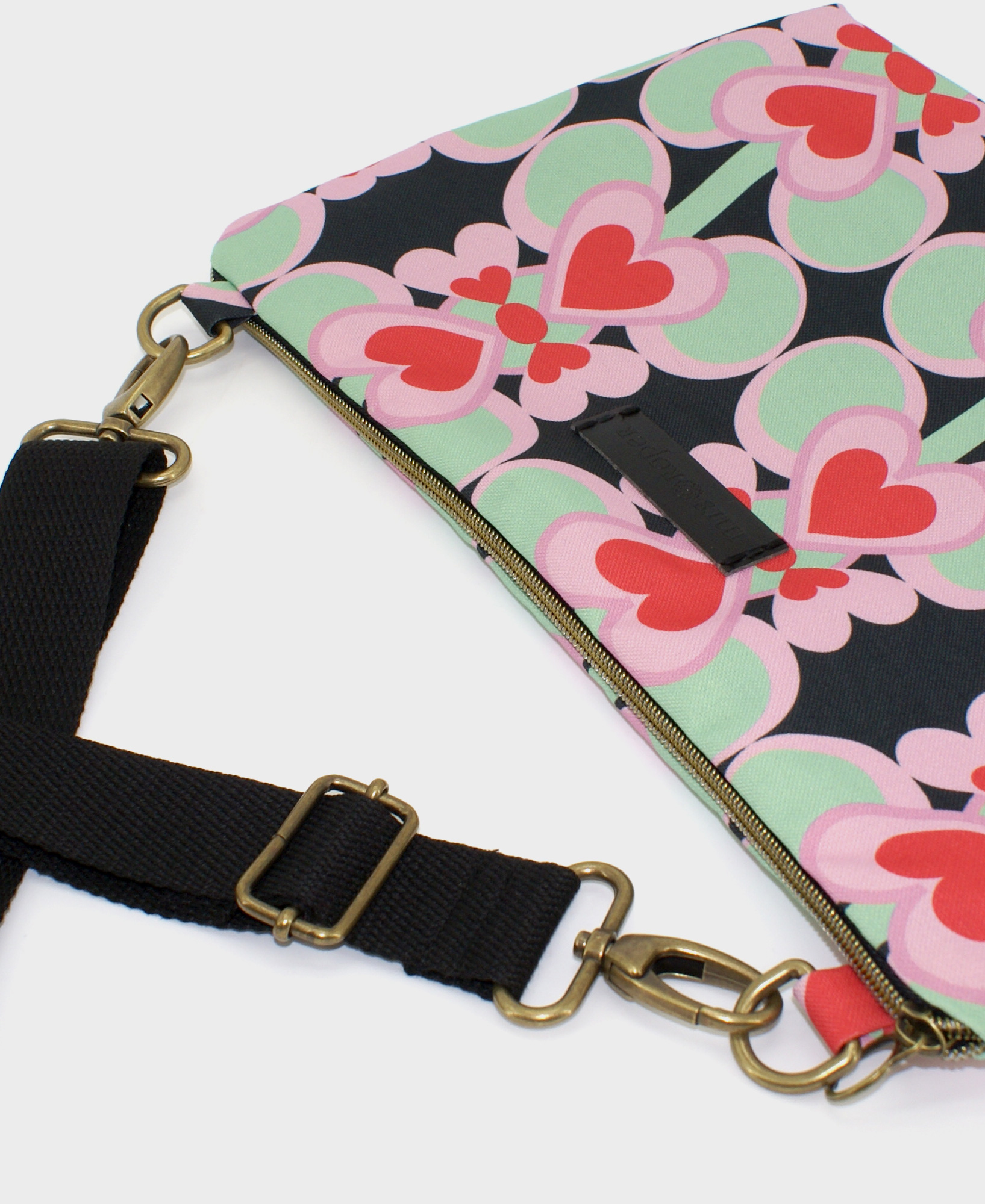 Bandolera mediana de mujer, realizada en tejido reciclado de botellas de plástico RPET, con estampado geométrico de corazones rojos sobre fondo negro, de la marca Mrs. Roper.