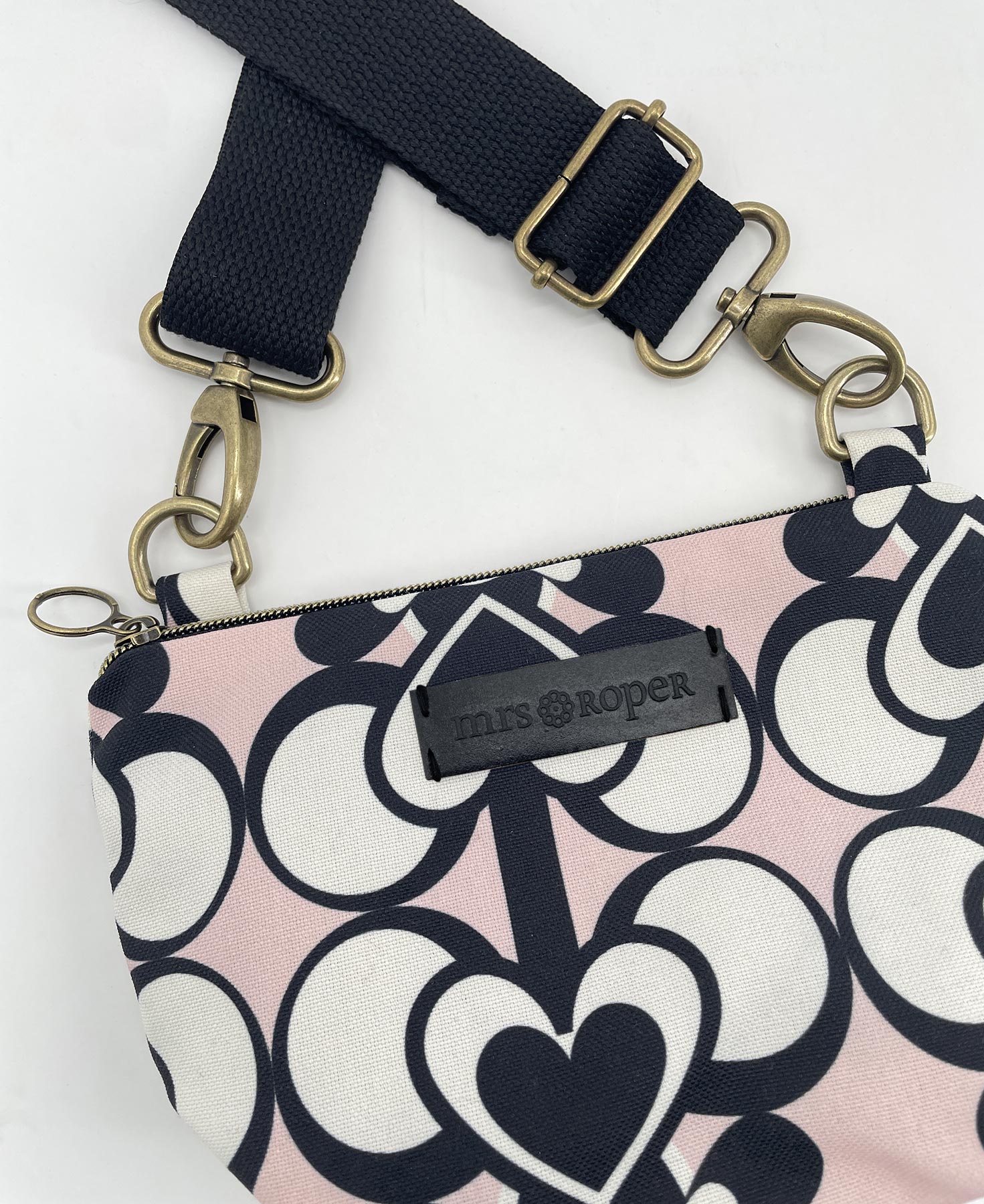 Bandolera pequeña de mujer realizada en tejido reciclado RPET con estampado geométrico de corazones en blanco y negro sobre fondo rosa, de la marca Mrs. Roper.
