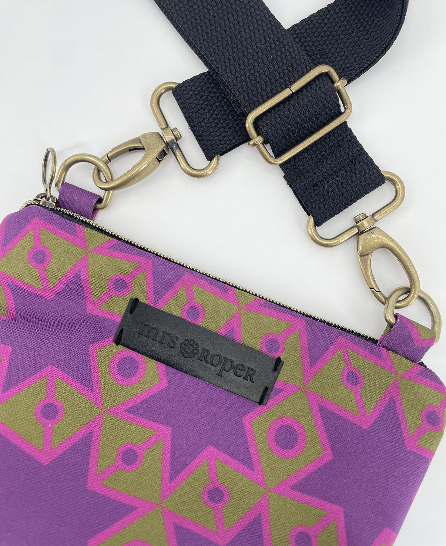 Bandolera pequeña de mujer realizada en tejido reciclado RPET con estampado geométrico de estrellas en morado sobre fondo verde, de la marca Mrs. Roper.