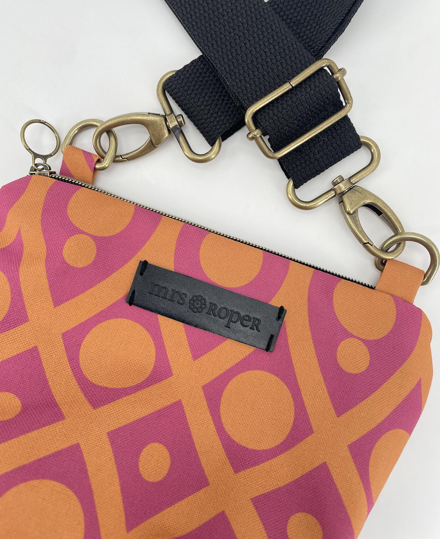 Bandolera pequeña de mujer realizada en tejido reciclado RPET con estampado geométrico naranja y fucsia, de la marca Mrs. Roper.