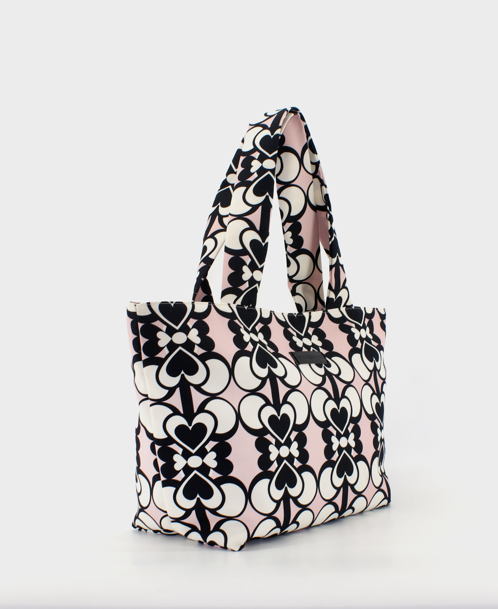 Bolso shopper mediano de mujer realizado en tejido reciclado RPET con estampado geométrico de corazones blancos y negros sobre fondo rosa, de la marca Mrs. Roper.