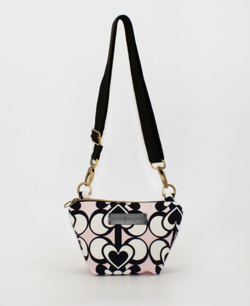 Bandolera pequeña de mujer, realizada en tejido reciclado RPET con estampado geométrico de corazones negros y blanco sobre fondo rosa, de la marca Mrs. Roper.
