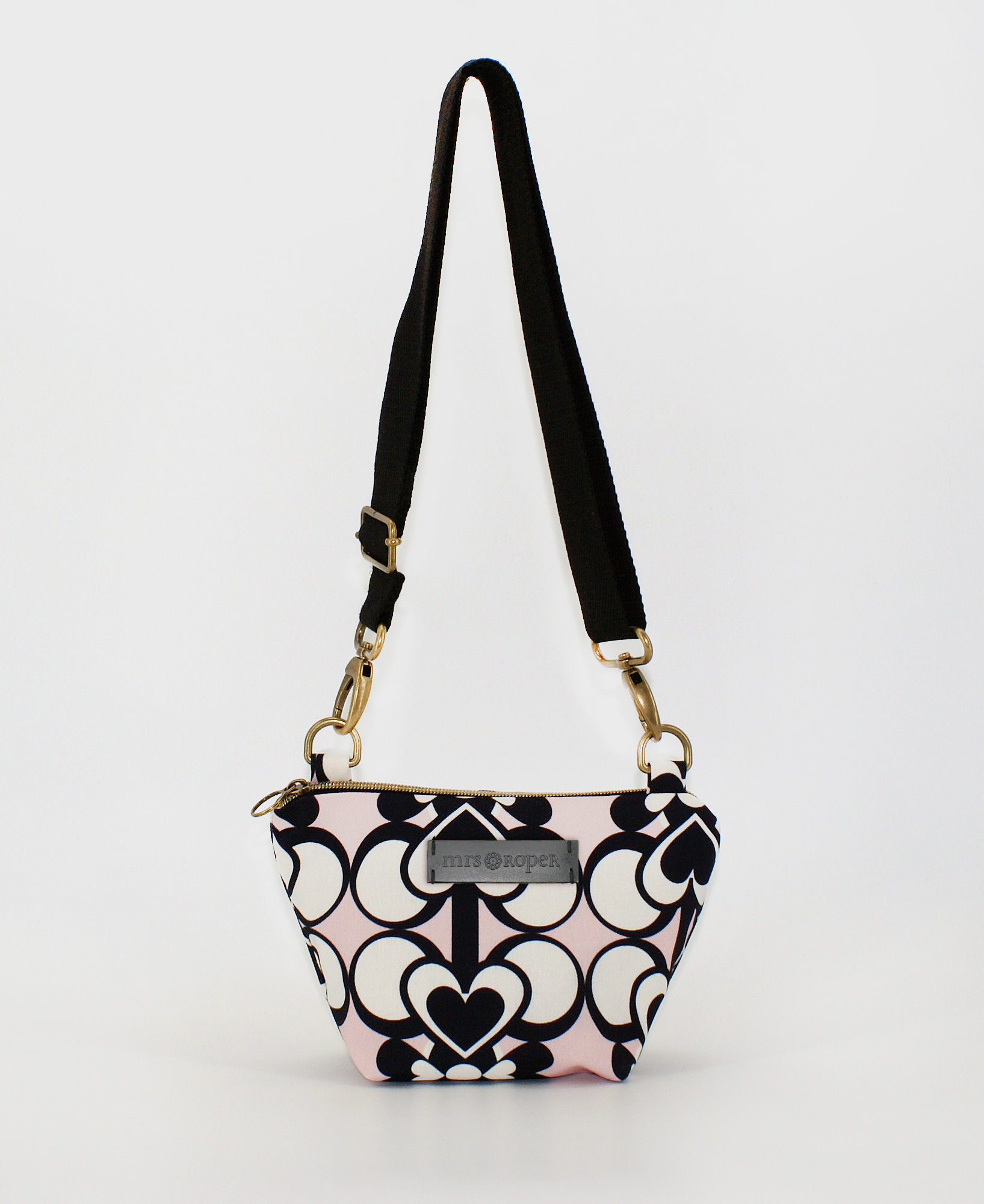 Bandolera pequeña de mujer, realizada en tejido reciclado RPET con estampado geométrico de corazones negros y blanco sobre fondo rosa, de la marca Mrs. Roper.